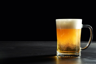 Photo of Glass mug with cold tasty beer on dark background