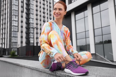 Photo of Woman sitting on parapet and tying shoelace of sneakers on street