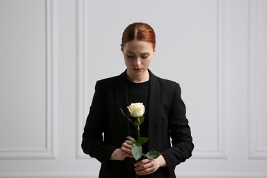 Sad woman with rose flower near white wall. Funeral ceremony