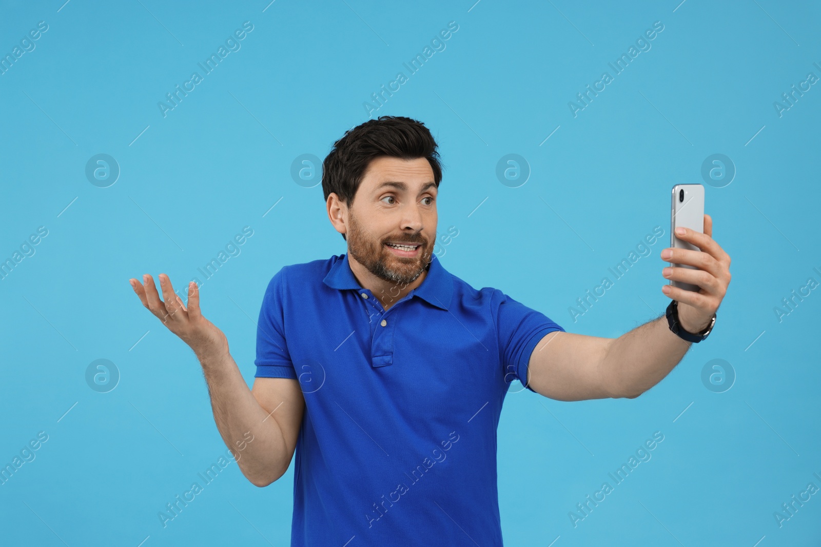 Photo of Puzzled man taking selfie with smartphone on light blue background