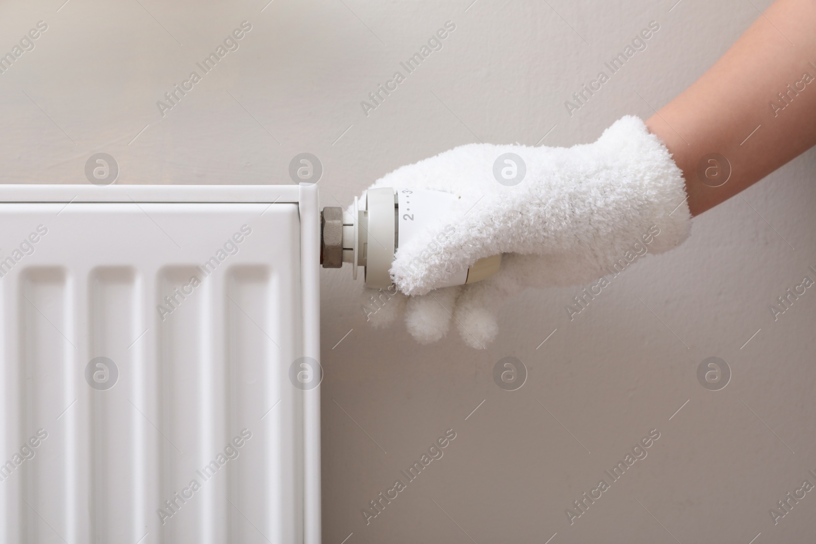 Photo of Girl in glove adjusting heating radiator thermostat near white wall, closeup