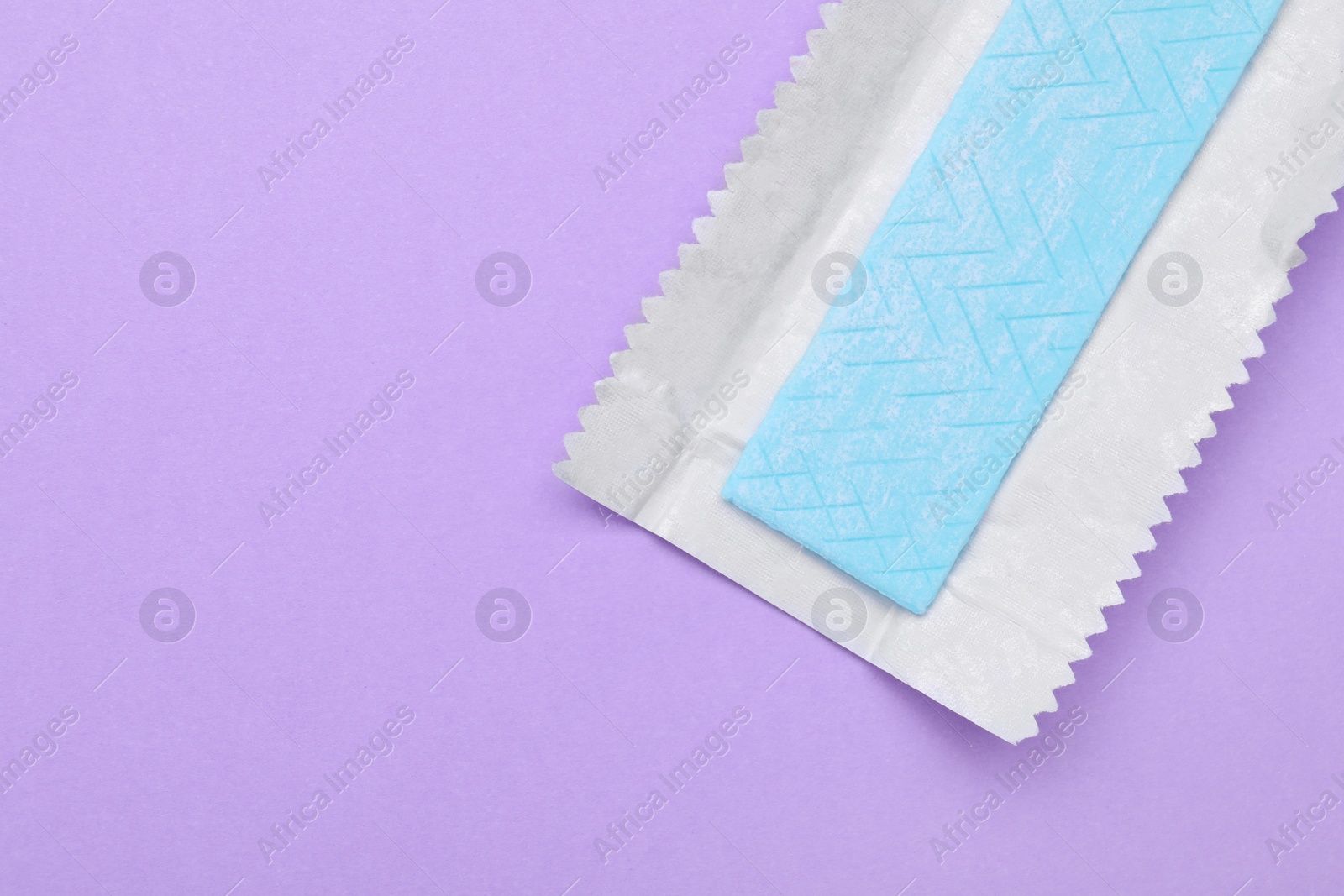 Photo of Unwrapped stick of chewing gum on violet background, top view. Space for text