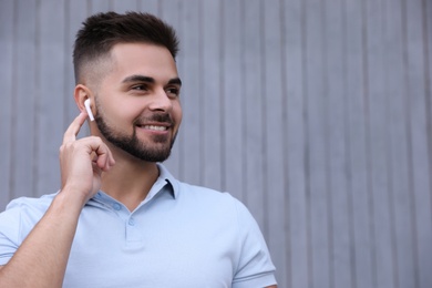 Photo of Young man with wireless headphones listening to music near grey wall. Space for text