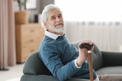 Photo of Portrait of happy grandpa with walking cane sitting on sofa indoors
