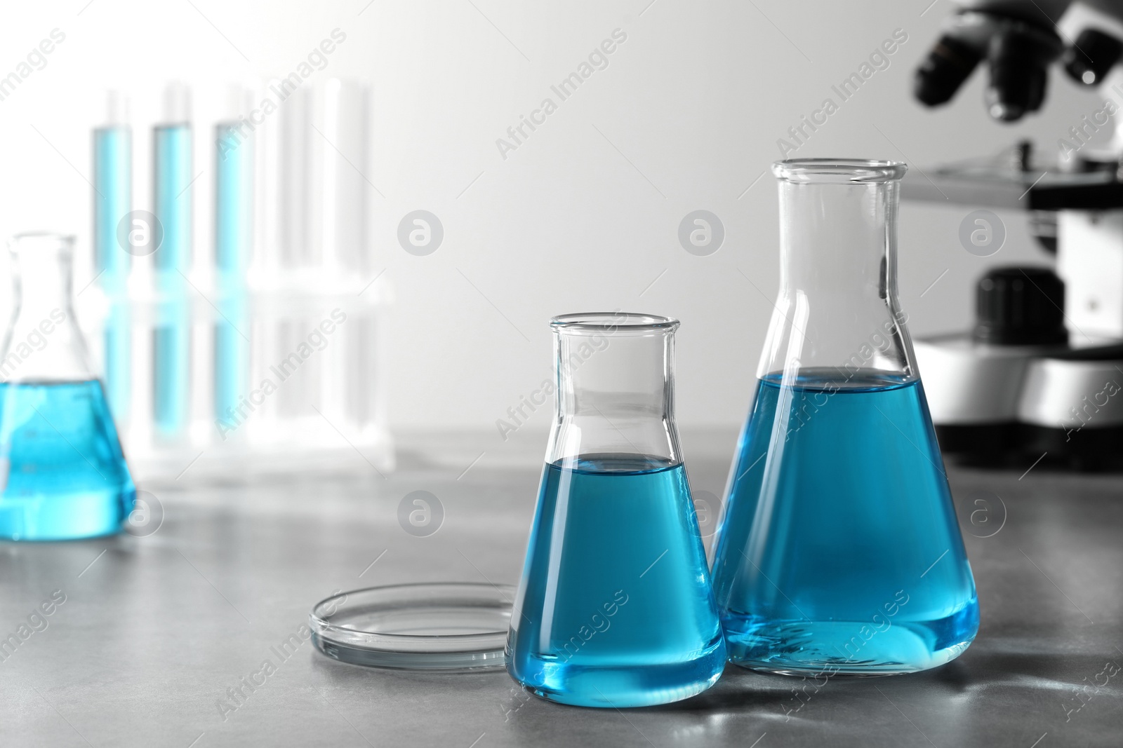 Photo of Different laboratory glassware with light blue liquid on table. Space for text