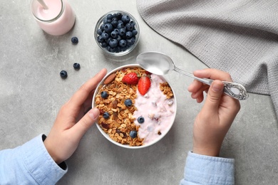 Photo of Woman eating tasty homemade granola with yogurt and berries at grey table, top view. Healthy breakfast