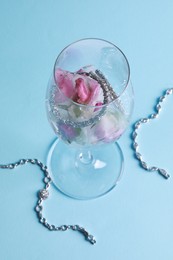 Photo of Elegant jewelry. Stylish presentation with luxury earrings, bracelets and frozen roses in glass on light blue background, above view