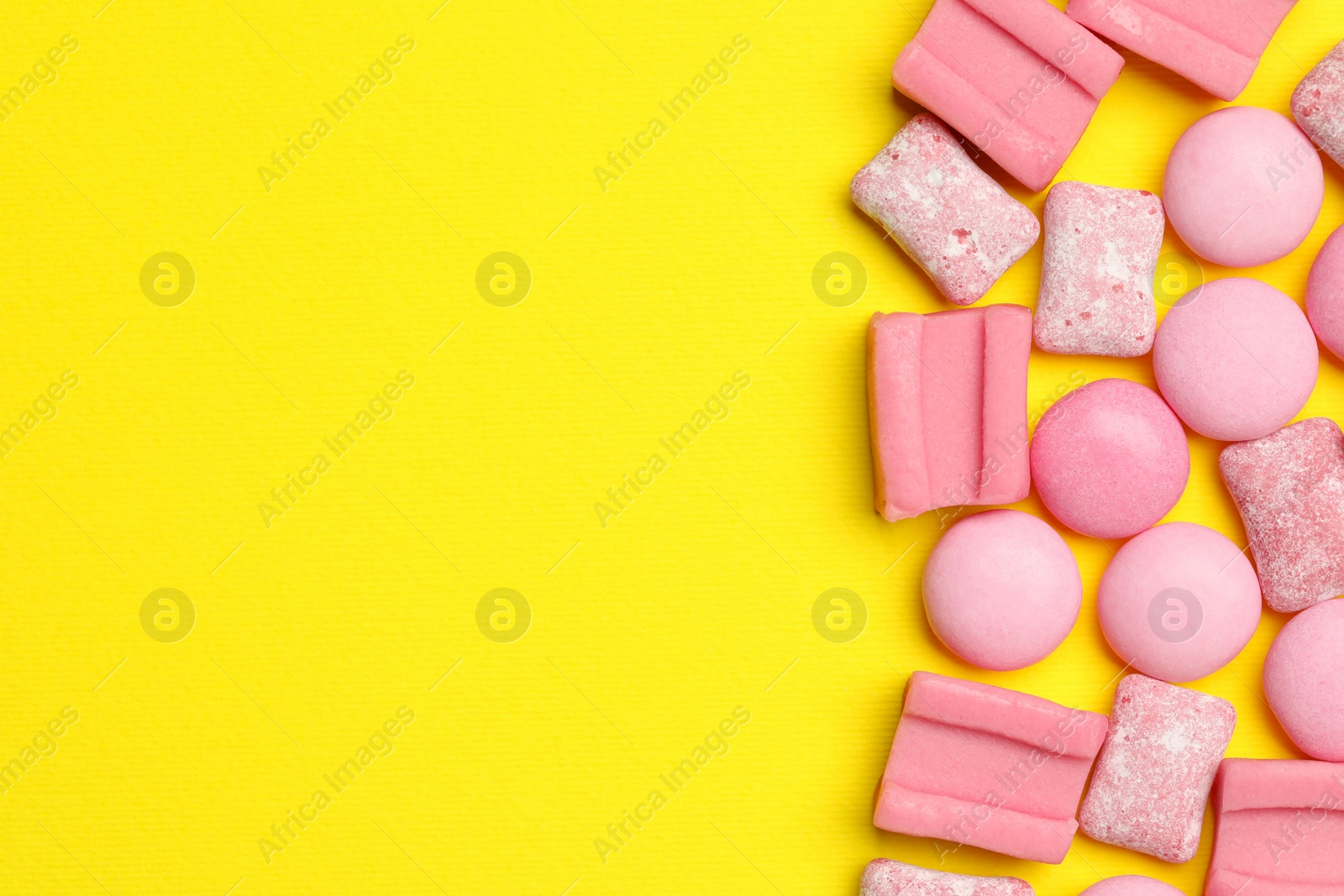 Photo of Pink bubble gums on yellow background, flat lay. Space for text