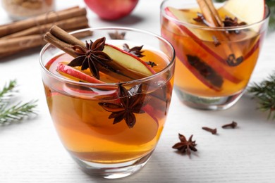 Photo of Hot mulled cider, ingredients and fir branches on white wooden table, closeup