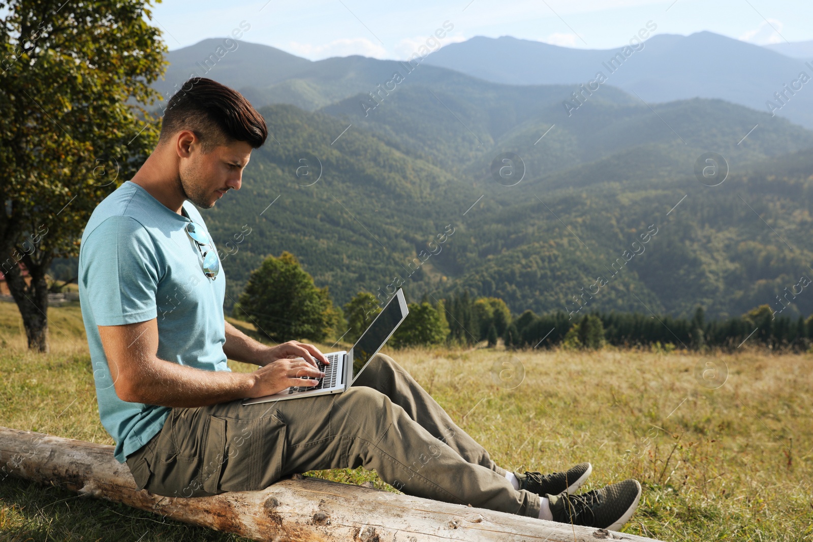 Photo of Man working with laptop in mountains on sunny day