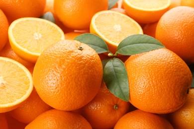 Photo of Cut and whole fresh ripe oranges with green leaves as background, closeup