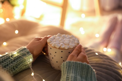 Photo of Woman holding cup of hot drink with marshmallows indoors, closeup. Magic Christmas atmosphere