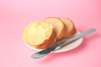 Photo of Slices of delicious baguette with butter and knife on pale pink background