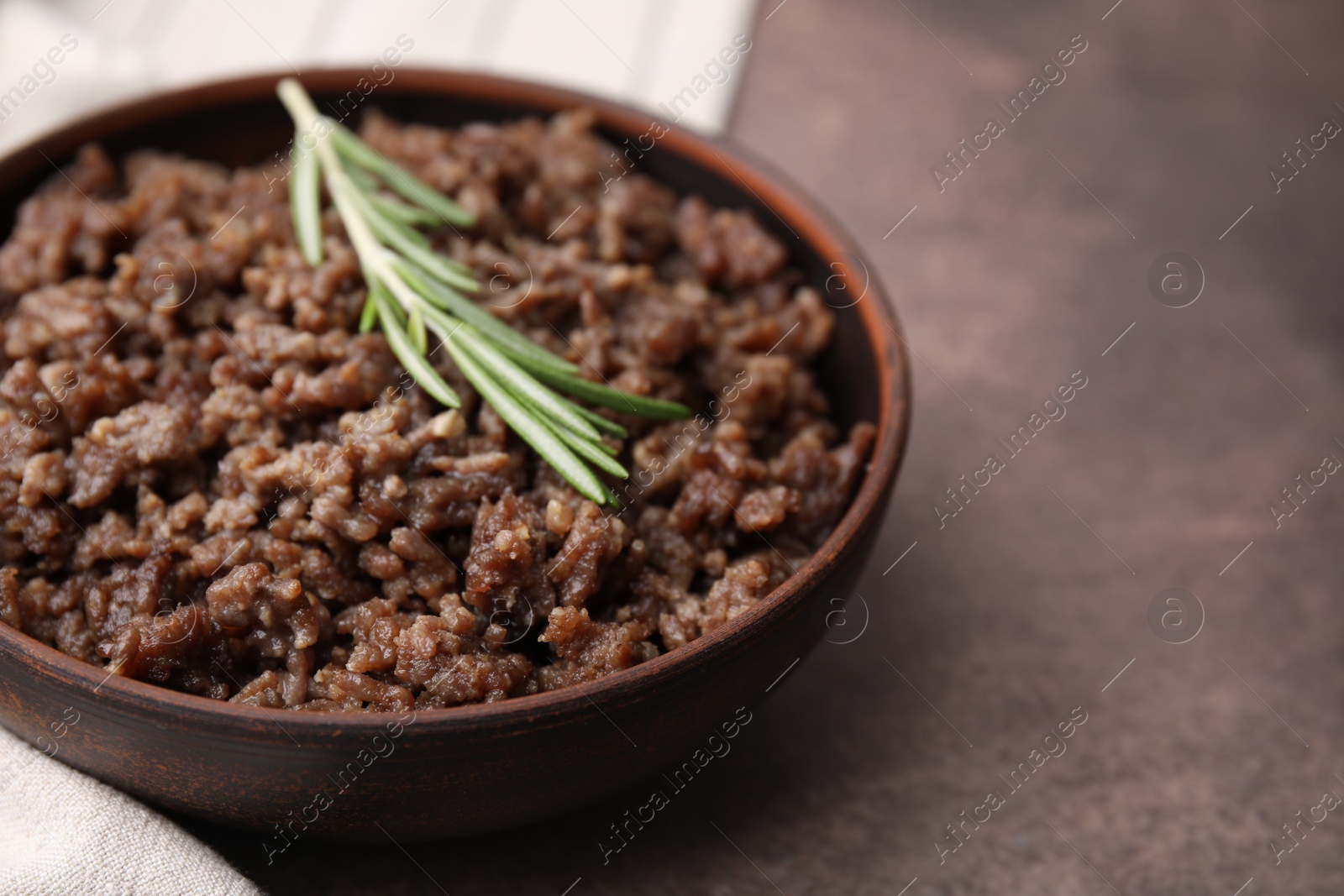 Photo of Fried ground meat in bowl and rosemary on brown textured table, closeup