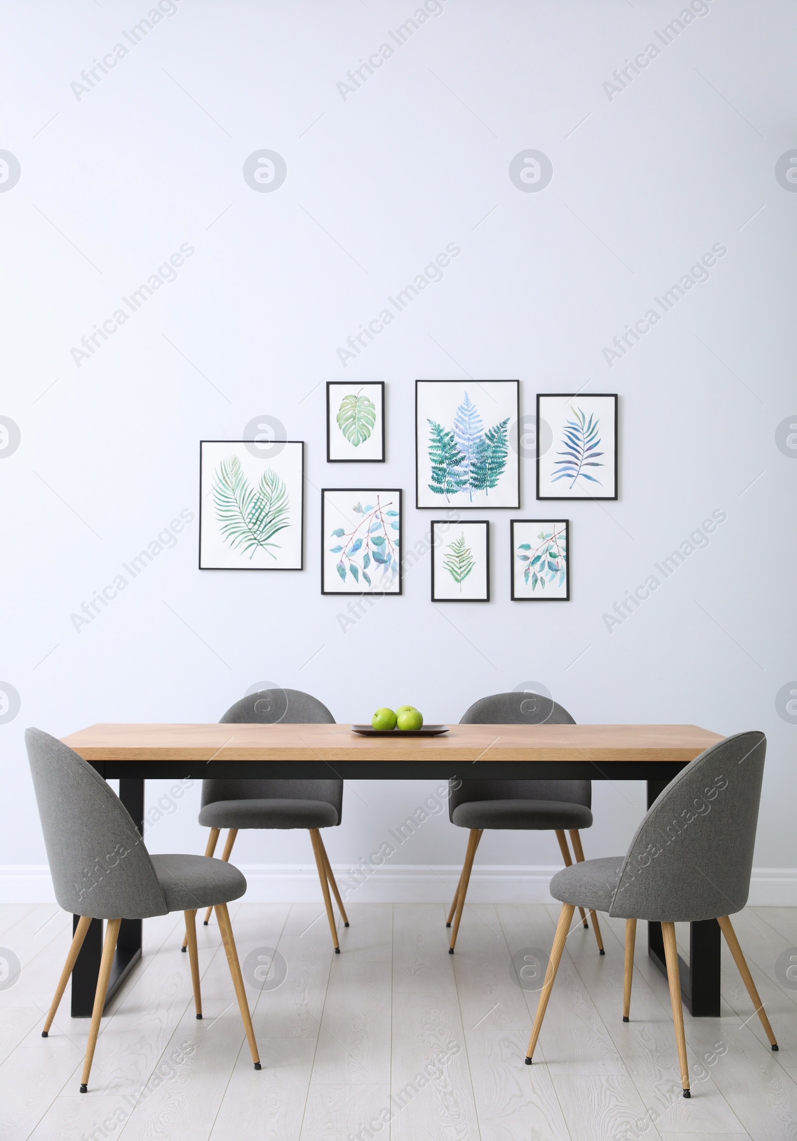 Photo of Stylish room interior with modern table, chairs and paintings of tropical leaves. Idea for design