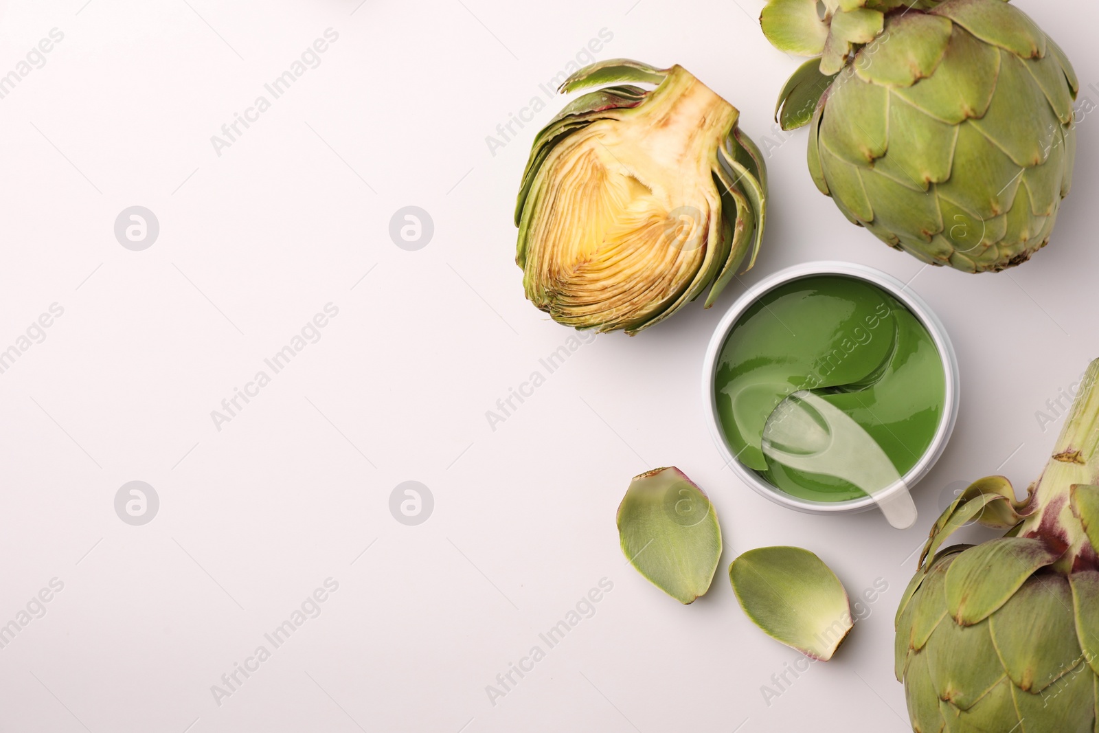 Photo of Package of under eye patches and artichokes on white background, top view. Cosmetic product