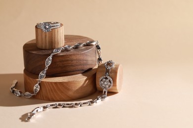 Photo of Stylish presentation of elegant bracelets and ring on wooden podiums, space for text. Luxury jewelry