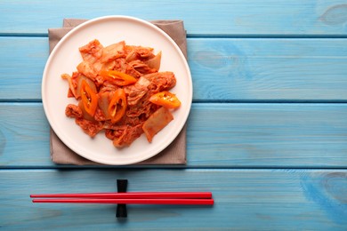 Plate of spicy cabbage kimchi with chili pepper and chopsticks on light blue wooden table, flat lay. Space for text