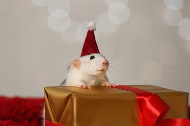 Cute little rat with Santa hat and gift box on fluffy blanket against blurred lights. Chinese New Year symbol