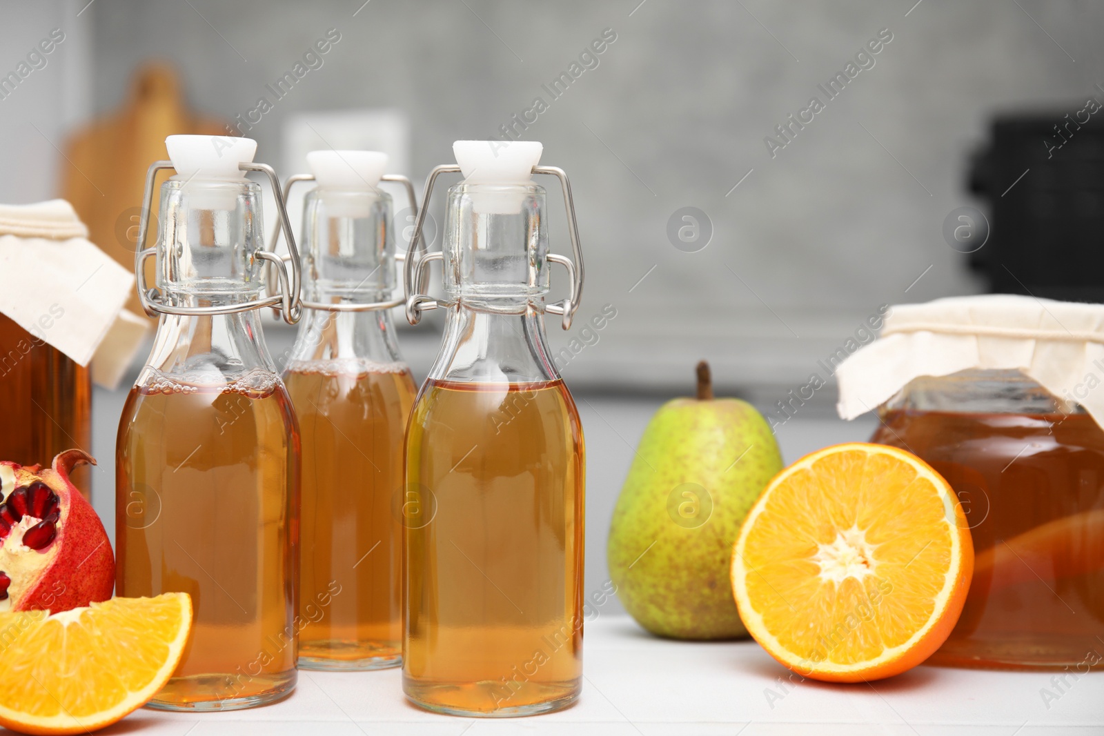 Photo of Homemade fermented kombucha in glass bottles and fresh fruits on white table in kitchen