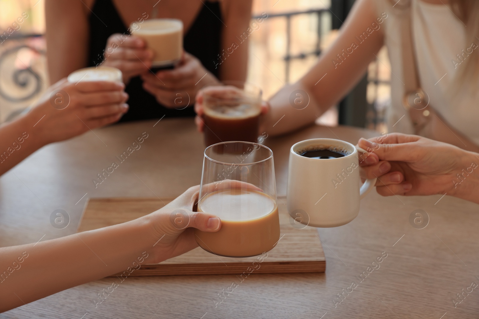 Photo of Friends drinking coffee at wooden table in cafe, closeup