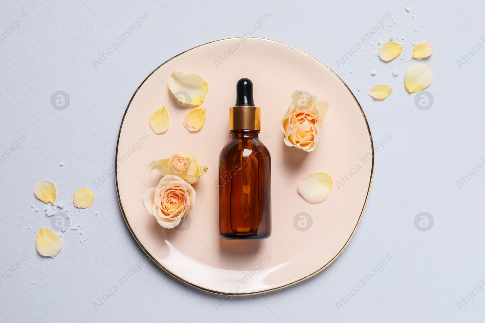 Photo of Bottle of cosmetic serum and beautiful flowers on light grey background, flat lay