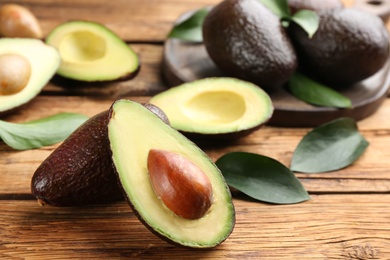 Photo of Whole and cut avocados with green leaves on wooden table, closeup