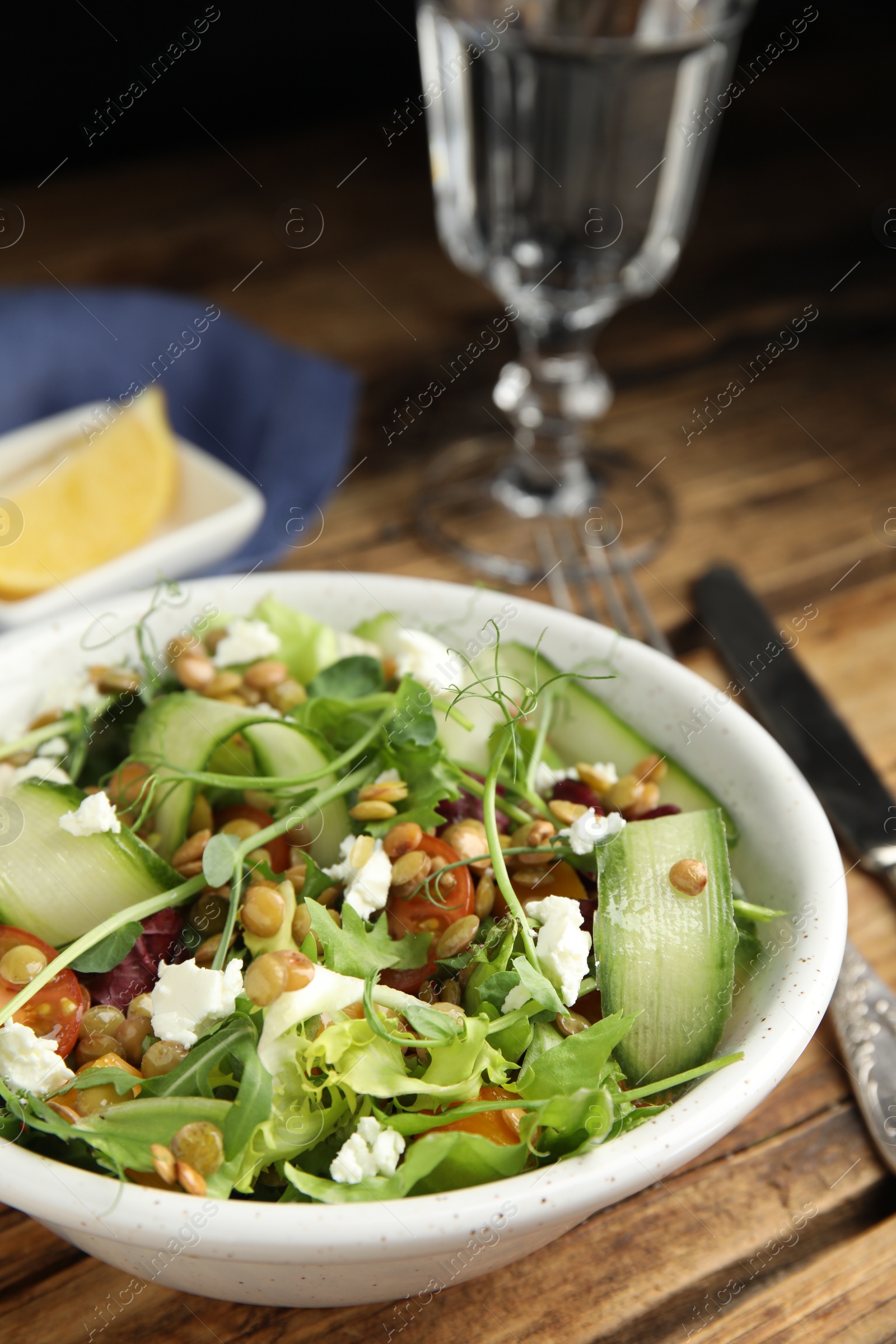 Photo of Delicious salad with lentils, vegetables and feta cheese served on wooden table
