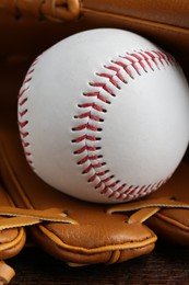 Leather baseball glove with ball on wooden table, closeup