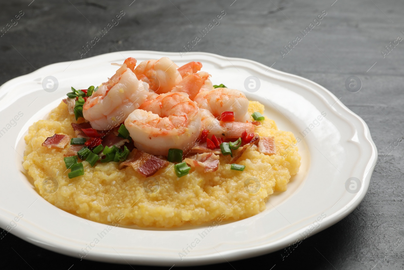 Photo of Plate with fresh tasty shrimps, bacon, grits, green onion and pepper on black table, closeup