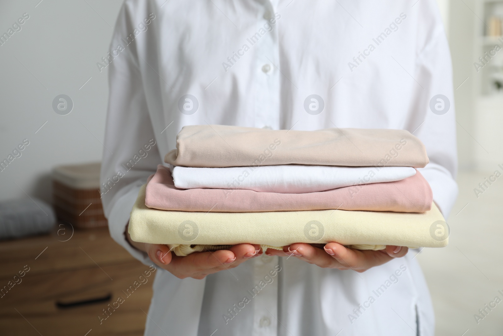 Photo of Woman holding folded clothes at home, closeup