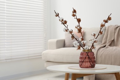 Cotton branches with fluffy flowers on white table in cozy room. Space for text