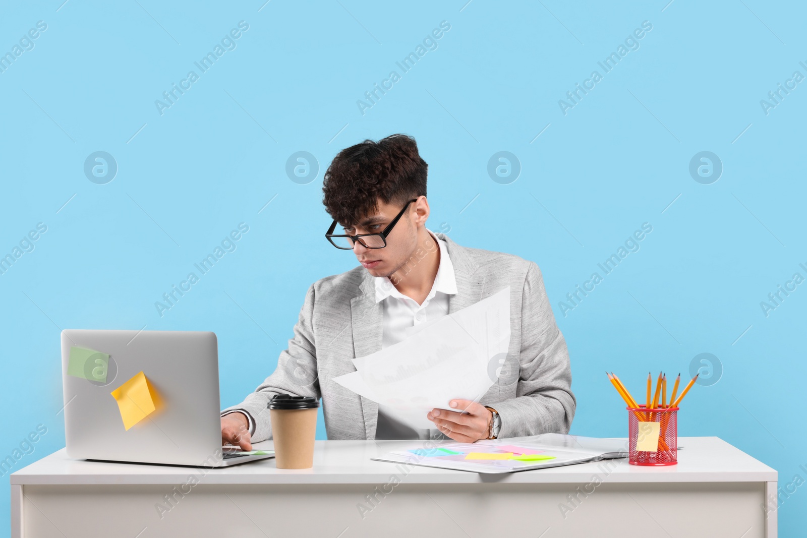 Photo of Young man working at white table on light blue background. Deadline concept