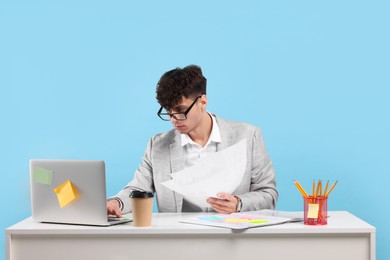 Photo of Young man working at white table on light blue background. Deadline concept