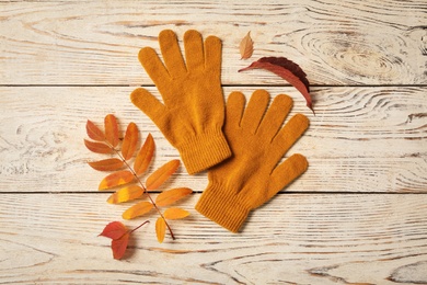 Photo of Stylish orange gloves and dry leaves on white wooden table, flat lay