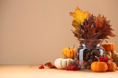 Photo of Composition with beautiful autumn leaves, berries and pumpkins on table against beige background, space for text