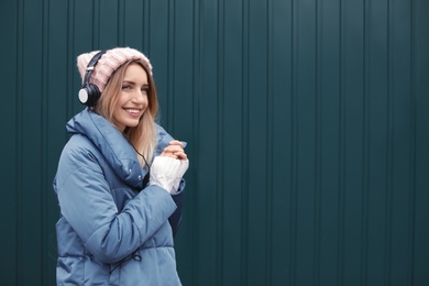 Young woman with headphones listening to music near color wall. Space for text