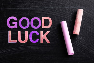 Image of Pieces of color chalk and phrase GOOD LUCK on blackboard, flat lay