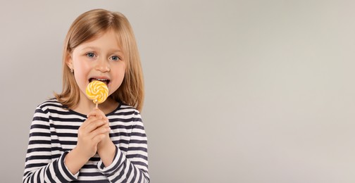 Photo of Portrait of cute girl licking lollipop on light grey background, space for text