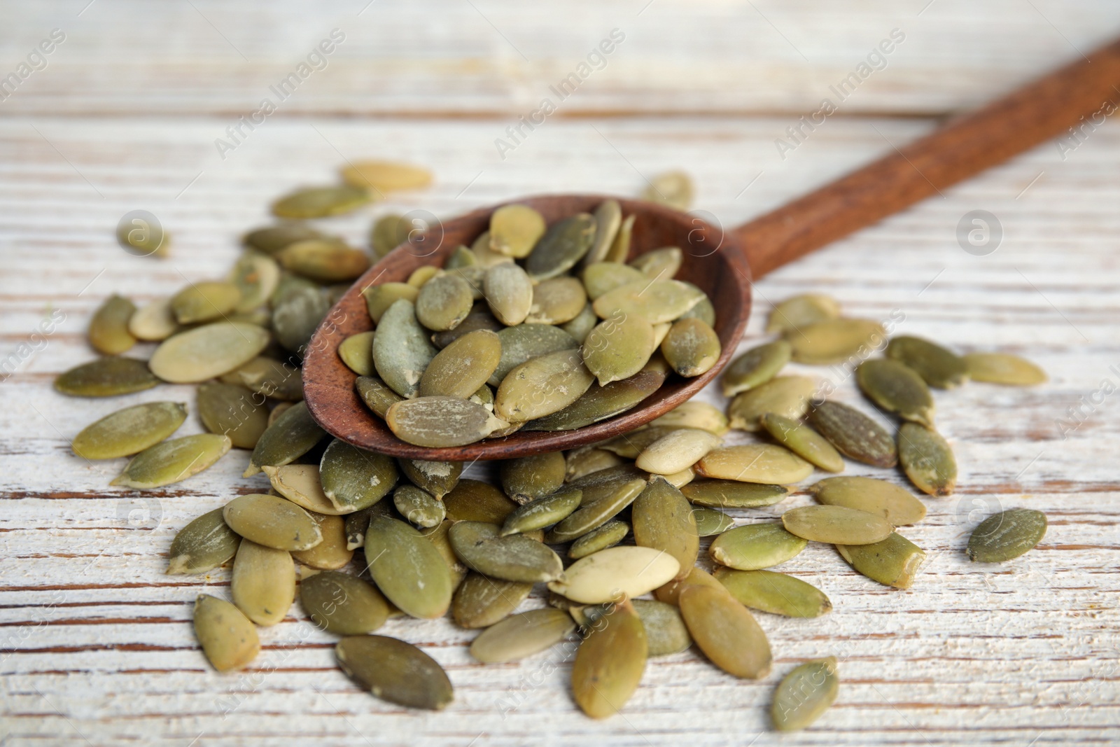 Photo of Spoon with pumpkin seeds on white wooden table, closeup