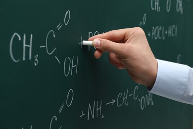 Photo of Teacher writing chemical formulas with chalk on green chalkboard, closeup