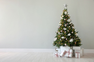 Photo of Beautiful decorated Christmas tree and gifts near light wall. Space for text