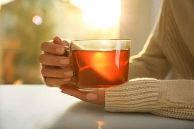 Photo of Woman holding glass cup of tea at table at home, closeup