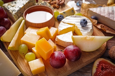 Photo of Board with different kinds of delicious cheese and snacks on wooden background, closeup