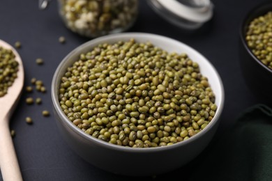 Photo of Different dishware with green mung beans on black background, closeup