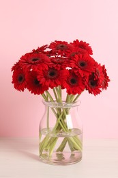 Photo of Bouquet of beautiful red gerbera flowers in glass vase on pink background