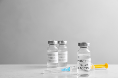 Photo of Chickenpox vaccine and syringe on white wooden table, space for text. Varicella virus prevention