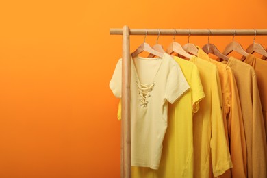 Rack with different stylish women's clothes near orange wall, space for text