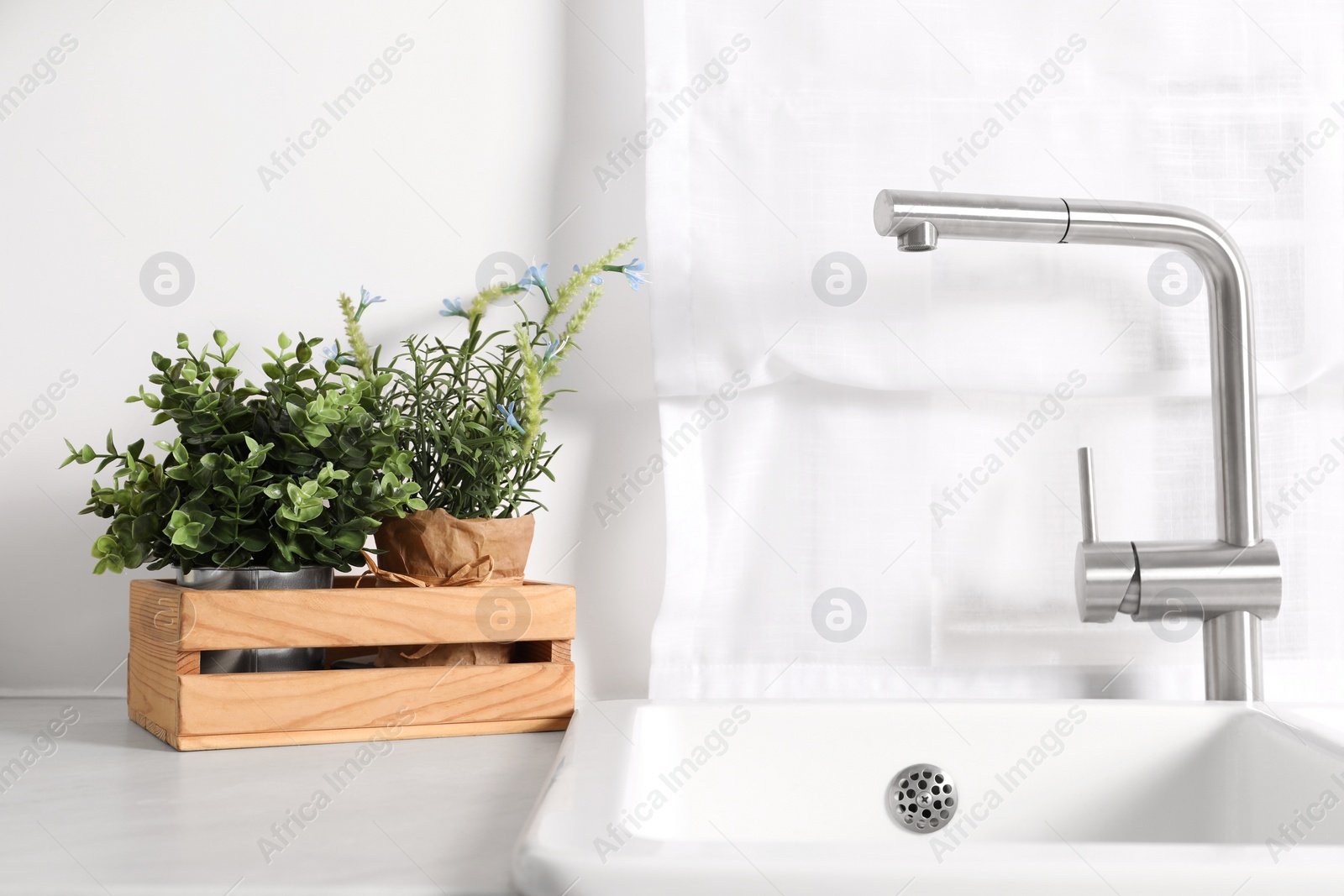 Photo of Artificial potted herbs on white marble countertop near sink in kitchen. Home decor