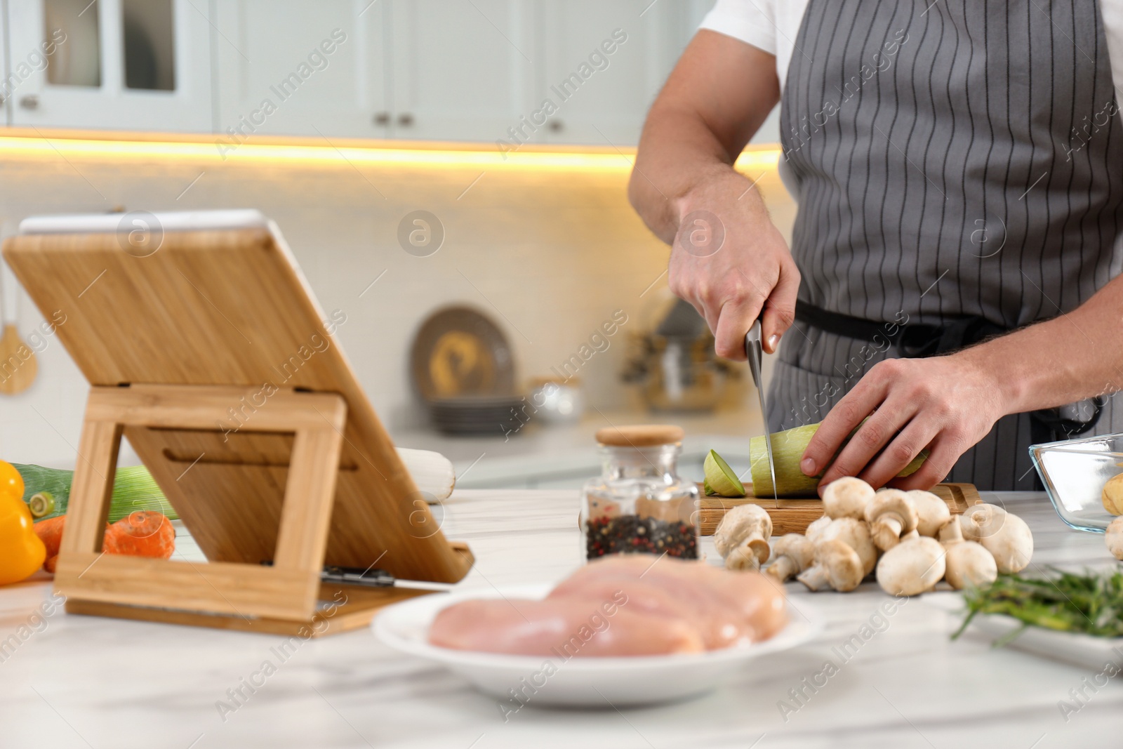 Photo of Man cutting zucchini while watching online cooking course via tablet in kitchen, closeup